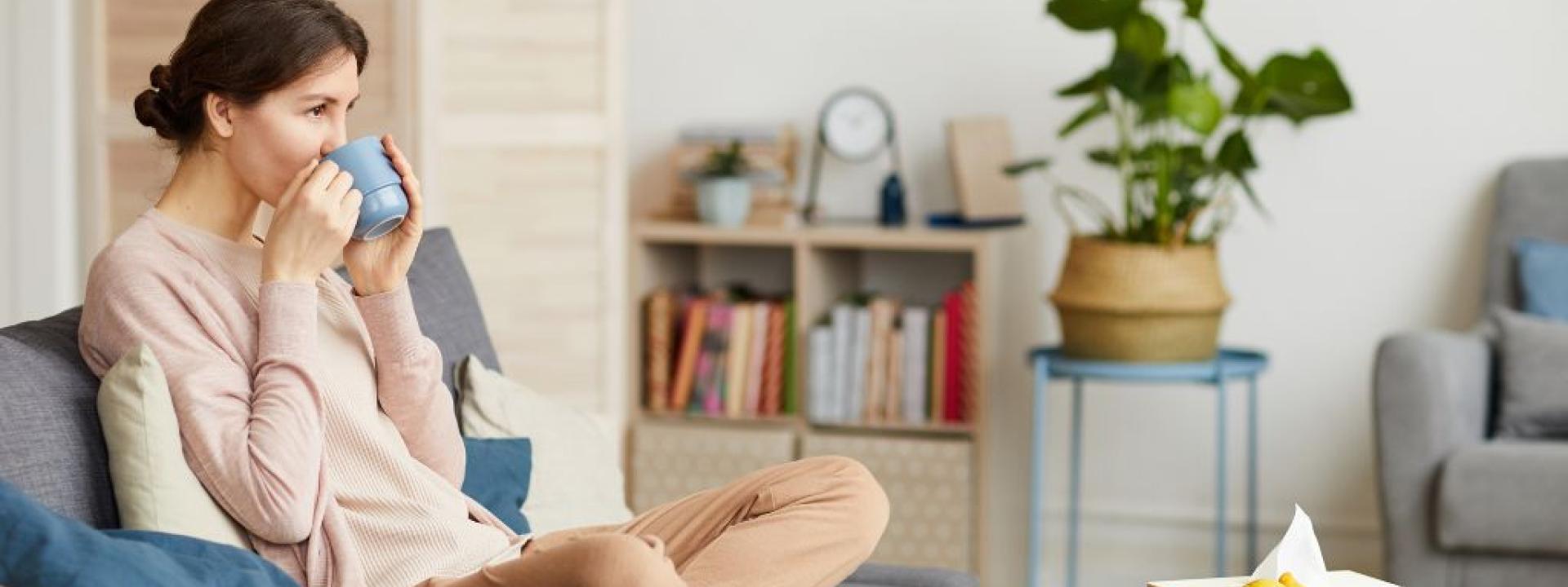 Woman on couch drinking from mug, recovering from oral surgery